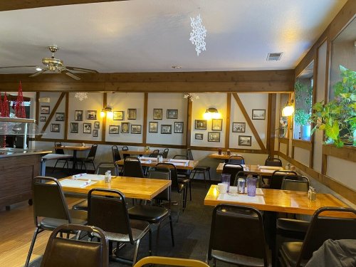 Cozy restaurant interior with wooden beams, tables set for dining, and framed photos on the walls.