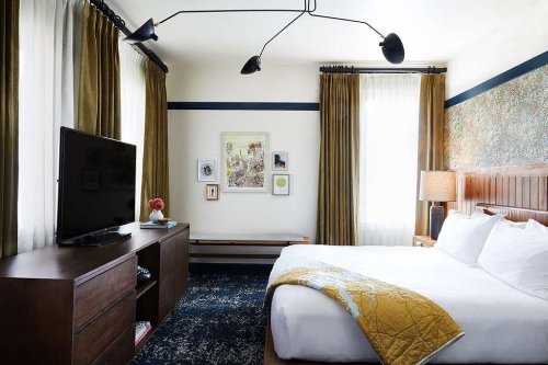 A cozy hotel room featuring a bed, TV, and stylish decor with curtains and artwork on the walls.