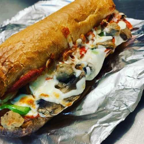 A toasted sub sandwich filled with melted cheese, mushrooms, peppers, and marinara sauce, wrapped in foil.