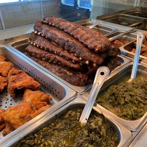 A display of delicious barbecue ribs stacked high, alongside fried chicken and greens in metal trays.