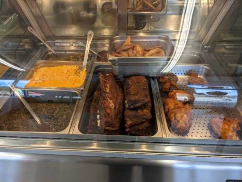 A display case filled with various cooked meats, including ribs, chicken wings, and sides like macaroni and greens.