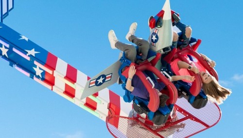 Two riders enjoy a thrilling upside-down ride on a colorful amusement park attraction against a clear blue sky.