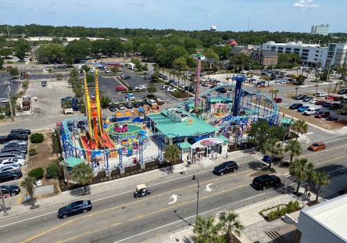 Aerial view of a colorful amusement park with rides, surrounded by parking lots and buildings on a sunny day.