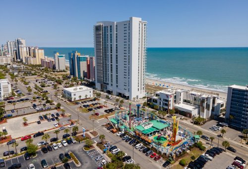 Aerial view of a beachside area with tall buildings, a colorful amusement park, and the ocean in the background.