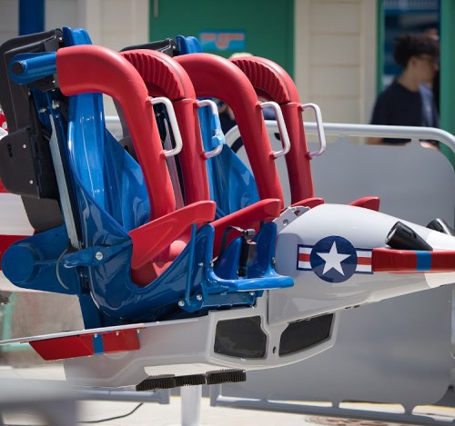 Close-up of colorful roller coaster seats in red, white, and blue, designed to resemble an aircraft.