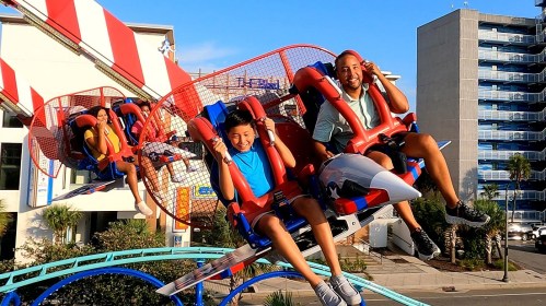 A child and an adult enjoy a roller coaster ride, smiling with excitement against a clear blue sky.