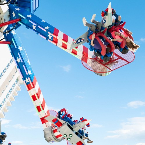 A thrilling amusement park ride with riders enjoying a spin against a blue sky, featuring red, white, and blue colors.