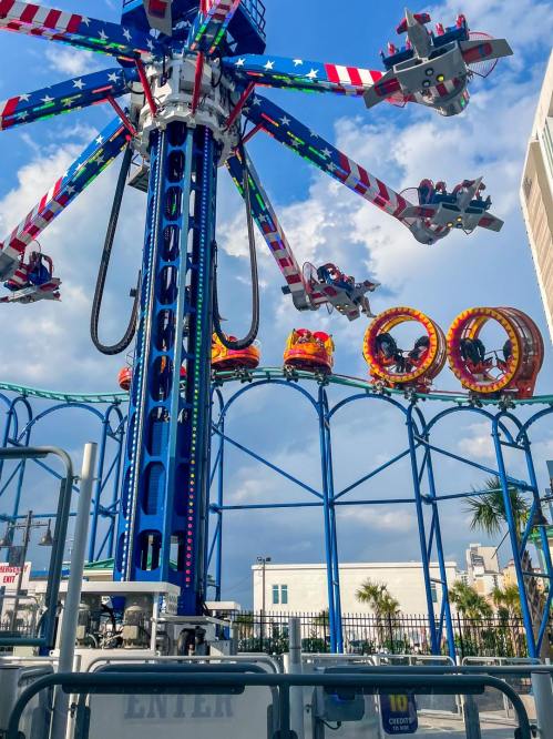 A colorful amusement park ride with spinning seats against a blue sky and clouds, surrounded by a festive atmosphere.