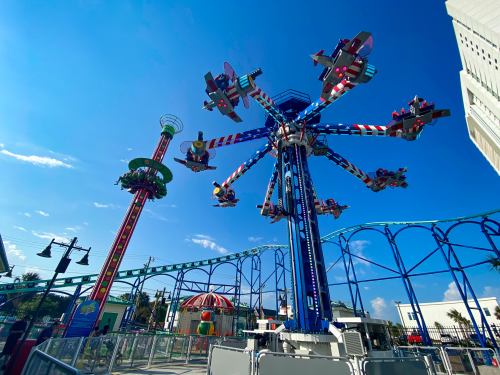 Colorful amusement park rides against a bright blue sky, featuring a swing ride and a spinning aircraft attraction.