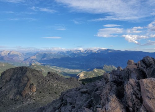 A panoramic view of mountains under a blue sky with scattered clouds, showcasing rocky terrain and distant peaks.