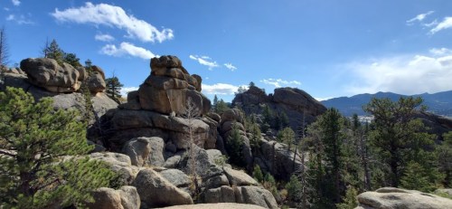 Rocky landscape with towering boulders, scattered trees, and a clear blue sky in the background.