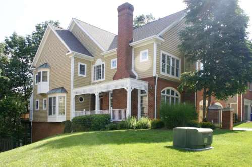 A large, two-story house with a porch, surrounded by greenery and a generator in the foreground.