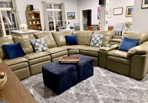 A cozy living room featuring a large leather sectional sofa with blue pillows, a coffee table, and a plush rug.