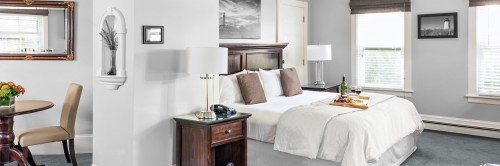 Cozy hotel room featuring a queen bed, dining table, and natural light from large windows.