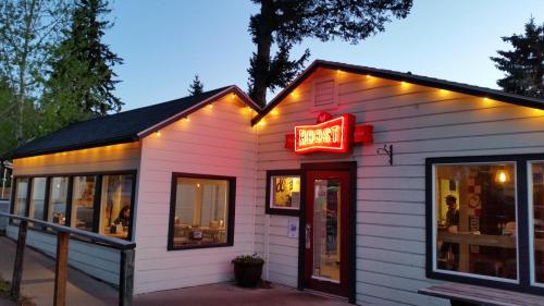 A cozy restaurant exterior with a bright red sign, warm lights, and large windows, surrounded by trees at dusk.