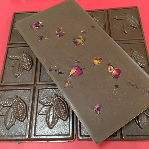 A chocolate bar with rose petals on top, resting on a textured chocolate background.