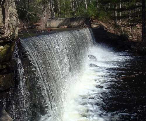 A serene waterfall cascading over a stone structure, surrounded by lush greenery and trees.