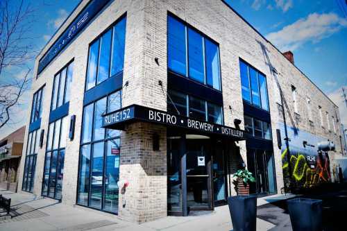Exterior view of a modern bistro, brewery, and distillery with large windows and a mural on the side.