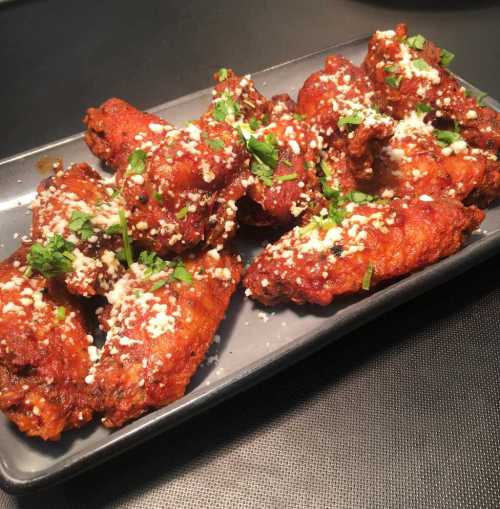 A platter of crispy chicken wings topped with herbs and sprinkled with cheese, served on a black plate.