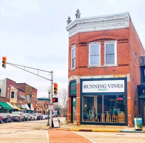 A brick building with "Running Vines Winery" sign, located at a street corner with traffic lights and nearby shops.