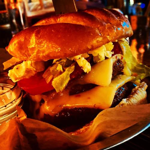 A close-up of a juicy burger with melted cheese, lettuce, tomato, and a toasted bun, served on a plate.