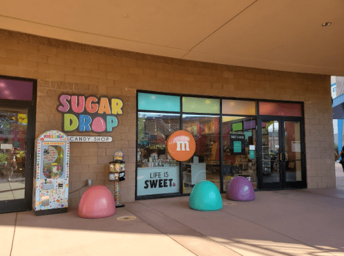 Colorful storefront of Sugar Drop Candy Shop with playful decor and large, pastel-colored seating outside.