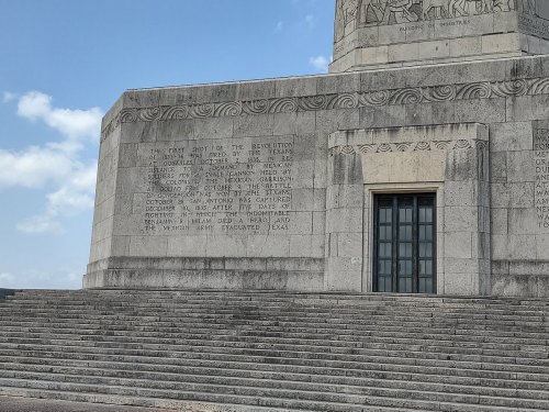 Close-up of a stone monument's base with engraved text and steps, under a blue sky with scattered clouds.