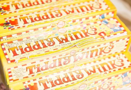 Colorful boxes of Tiddlywinks game stacked together, featuring playful designs and text on the packaging.