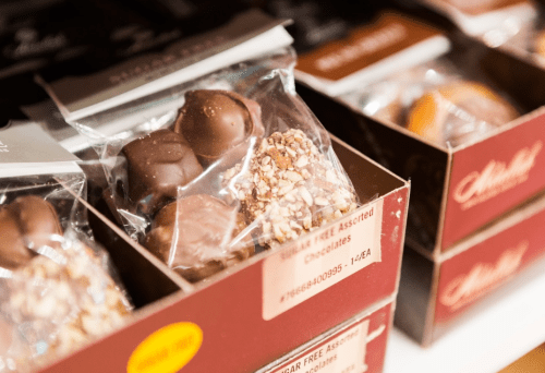 Assorted chocolates in clear packaging, displayed in brown boxes on a shelf.