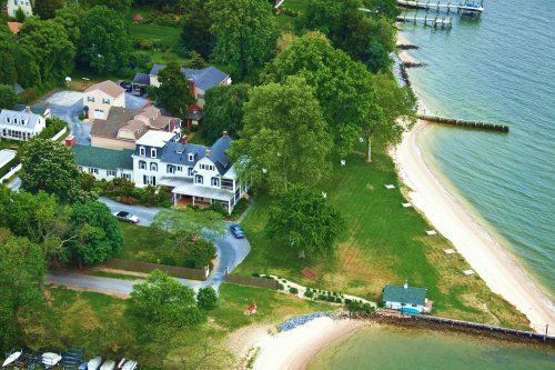 Aerial view of a coastal neighborhood with houses, trees, and a sandy beach along the water's edge.