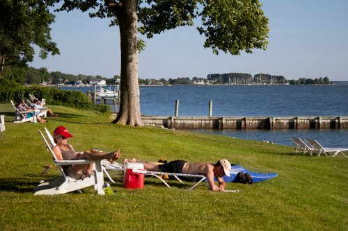Two people relax on lounge chairs by a lake, enjoying the sunny weather and scenic view.
