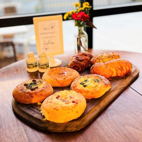 A wooden platter with various baked goods, including savory pastries and rolls, alongside a small vase of flowers.