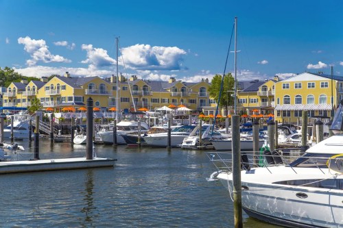 A marina with boats docked, surrounded by yellow buildings and blue skies with fluffy clouds.
