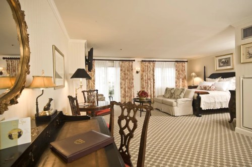 Elegant hotel room featuring a desk, seating area, and a king-sized bed with floral decor and natural light.