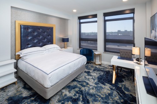 Modern hotel room featuring a queen bed, stylish decor, large windows, and a desk with a chair.