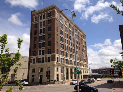 A tall, historic brick building with large windows, situated at a street corner under a partly cloudy sky.