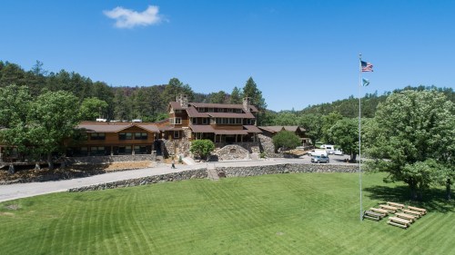 A large lodge surrounded by trees, with a grassy area in front and an American flag flying nearby.