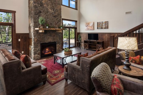 Cozy living room with a stone fireplace, comfortable sofas, and large windows overlooking nature. Warm and inviting decor.