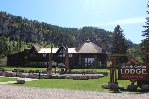 A large lodge surrounded by trees and mountains, with a sign indicating rooms are available.