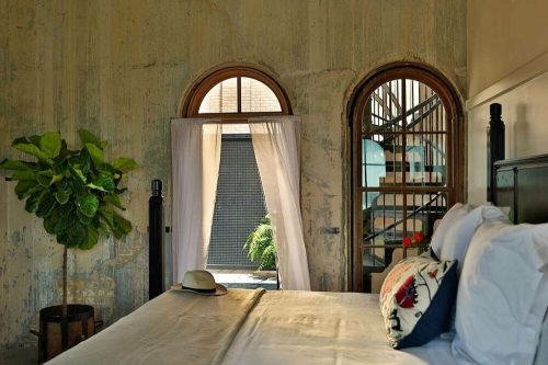 A cozy bedroom with a bed, a potted plant, and arched windows leading to a staircase and outdoor view.