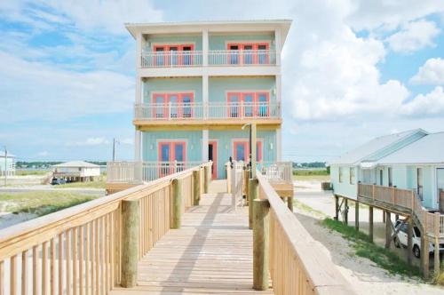 A beach house with a wooden walkway, featuring multiple balconies and bright orange accents under a blue sky.