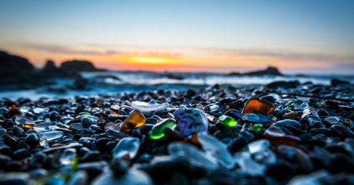 Several colorful pieces of sea glass on a beach in Oregon at sunset.