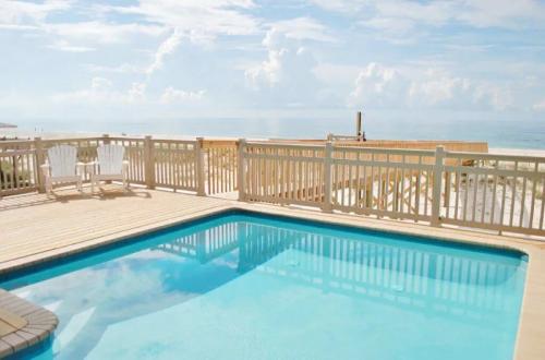 A serene poolside view with wooden deck, overlooking the ocean and a cloudy sky. Two chairs are visible nearby.