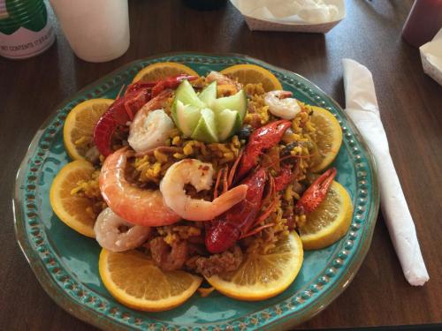 A colorful seafood dish with shrimp, lobster, and rice, garnished with lime and served on a plate with orange slices.