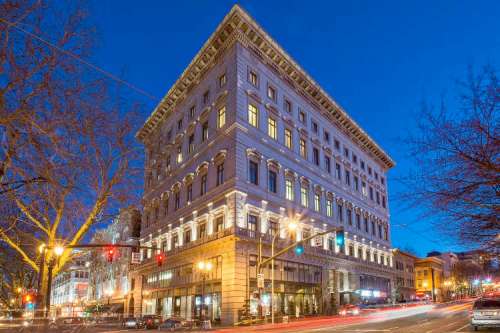 Historic building at dusk, featuring ornate architecture and illuminated streetlights, with light trails from passing cars.