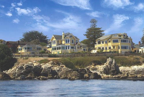A scenic view of yellow coastal houses on a rocky shore under a blue sky with scattered clouds.