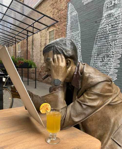 A bronze statue of a man with a cigar, sitting at a table with a drink, focused on a canvas in front of him.