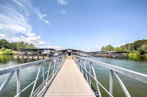 A wooden dock extends over calm water, leading to boat slips under a clear blue sky with scattered clouds.