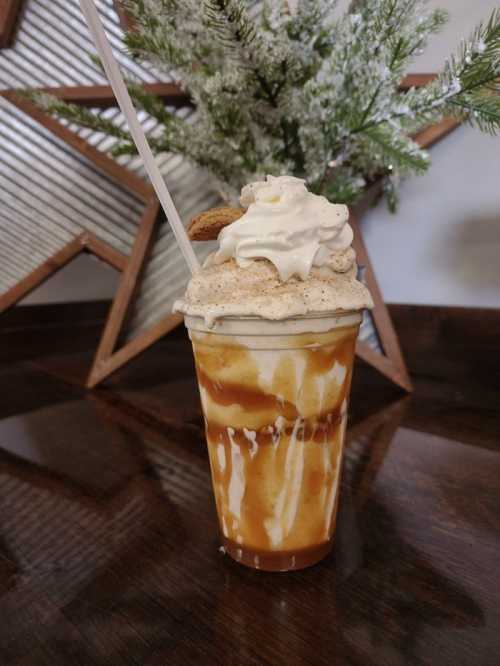 A tall cup of caramel milkshake topped with whipped cream and a cookie, set against a festive background.