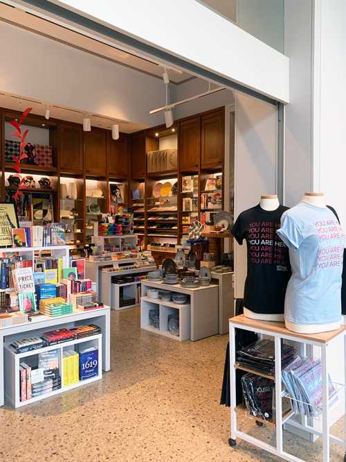 A cozy bookstore interior featuring shelves of books, gifts, and clothing displays with colorful merchandise.